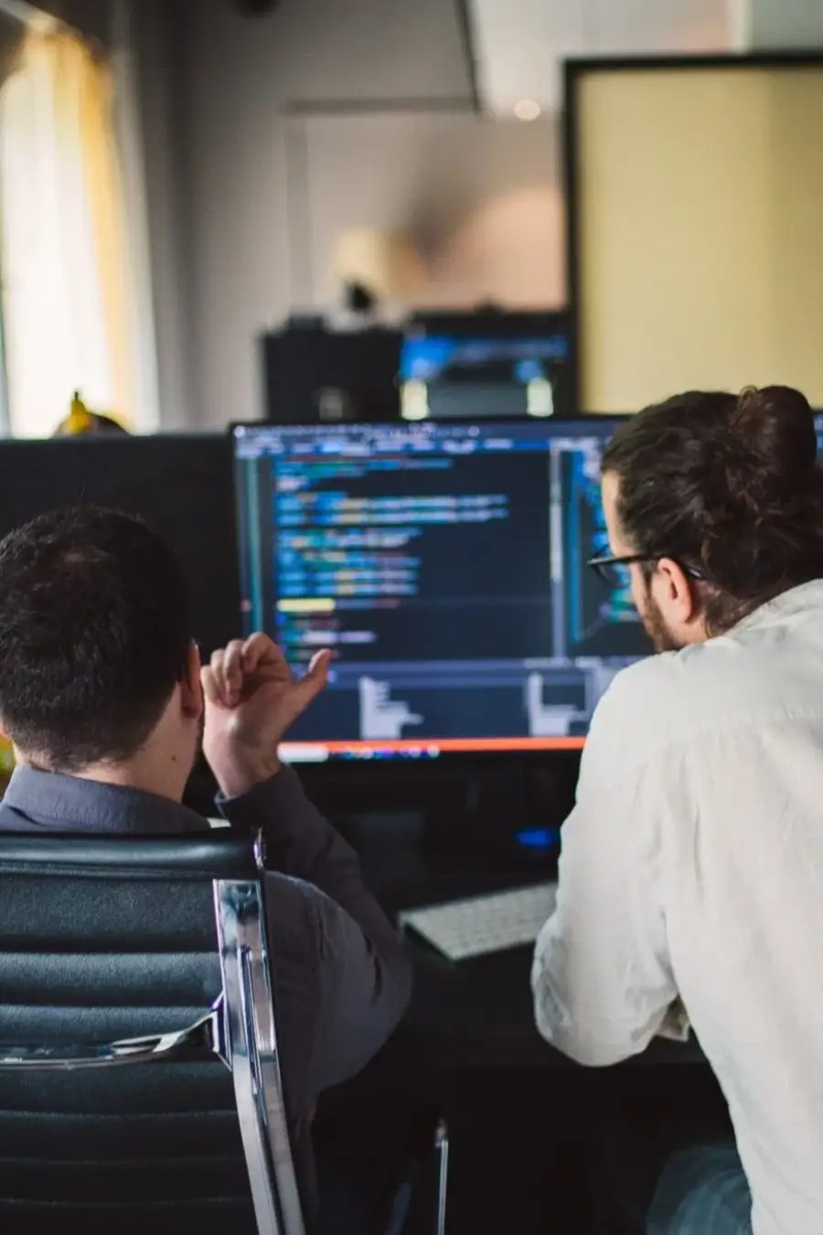 Two engineers at a shared desk, reviewing code on screen